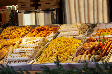 Food counter: French fries, sausages, hot dogs in boxes. Street food. Closeup.