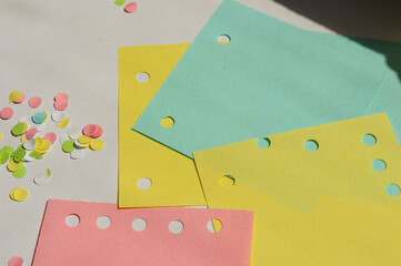 A hand using a blue paper hole puncher on a stack of colored sticky notes. Office and stationery...