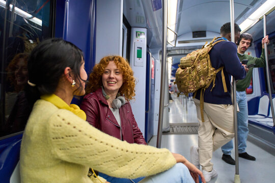 Two smiling women talking on subway train during commute