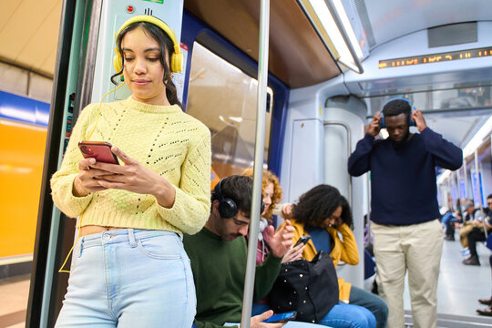 Young woman using smartphone and wearing headphones on subway train