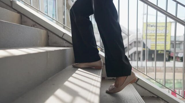 A woman is walking up the stairs. She is wearing black pants and a white shoe. The stairs are made of concrete