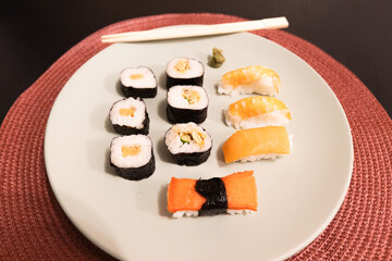 Delicious selection of fresh Japanese sushi rolls (maki) and sashimi slices beautifully presented on a plate with chopsticks.