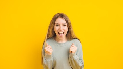 Excited young woman celebrating success on vibrant yellow background