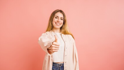 Fototapeta premium Young woman showing thumbs up sign on pink background