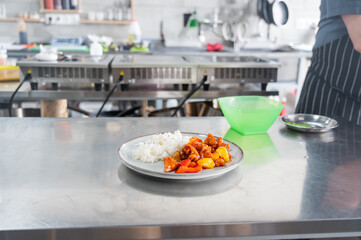 The chef prepares pork in sweet and sour sauce with boiled rice. 