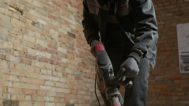 Low angle tilt up shot of African American workman wearing helmet and respirator destroying cement floor at worksite