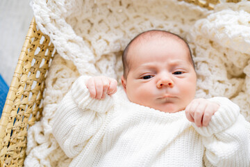 Closeup of cute newborn baby boy in light clothes at home. Eco Baby bed. Home.