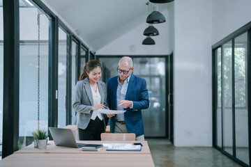 Senior manager explaining marketing strategy to young businesswoman in a modern office, reviewing documents and analyzing financial charts for a business project