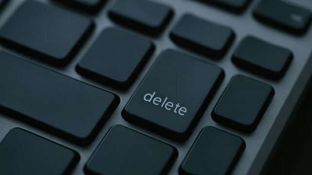 Finger presses delete key on black keyboard symbolizing digital termination and control in computer technology input and data management tasks