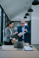 Senior businessman and businesswoman reviewing contract and discussing terms of agreement in modern...