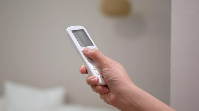 Turn-on the air conditioner by using the remote control, close-up and selective focus at human hand.
