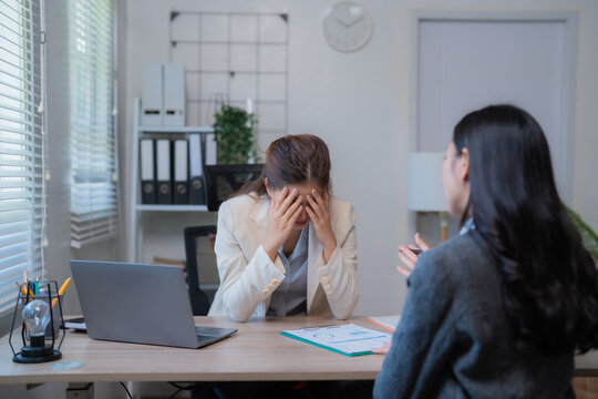 Business woman is stressed and covering her face with her hands while her colleague is comforting her at the office desk, showing support and empathy in a challenging work environment