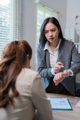 Impatient businesswoman is checking the time on her smartwatch during a meeting with a colleague,...