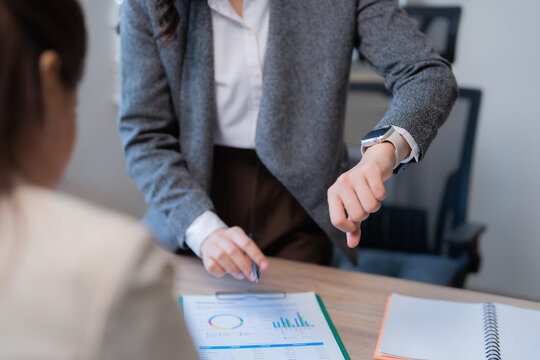 Businesswomen having a meeting about financial reports, one is pointing at the charts with a pen and the other is checking the time on her smartwatch