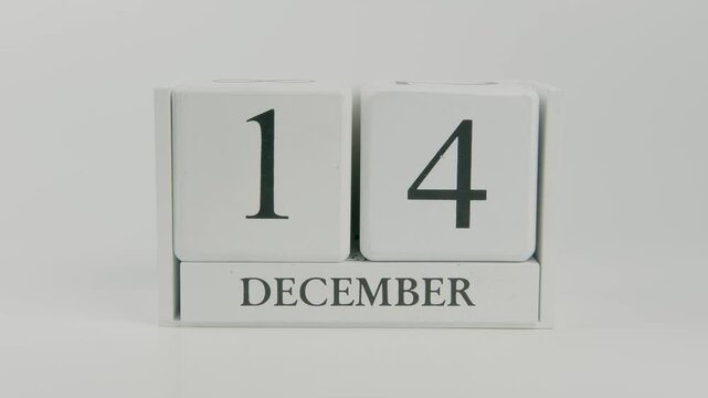 A hand flips a wooden calendar from December 14th to December 15th on a white background, signaling the start of a new day and marking the shift in time