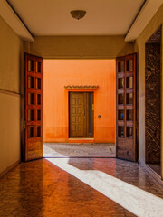 Open double wooden doors leading to a small courtyard with another wooden door at the end, Ferrara, Italy. The doors are crafted from rich, dark wood with decorative carvings.