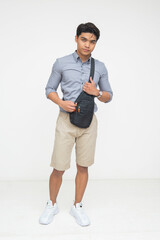 Southeast Asian man poses confidently while holding a black crossbody sling bag, showing relaxed...