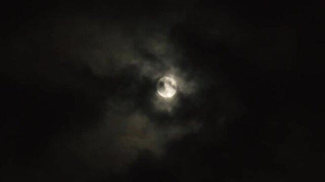 Night gloomy sky with full moon. Black clouds fly in front of the moon, like in thrillers, causing horror. Real video shooting of black night cloudy sky