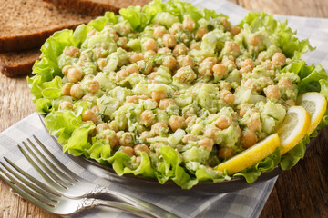 Vegan salad of chickpeas, celery, avocado, onion and lettuce served with whole grain bread close-up in a plate on the table. Horizontal
