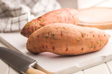 Raw sweet potatoes on cutting board on white table.