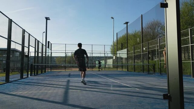 Smooth gimbal shot of four players competing on a blue outdoor padel court, captured in dynamic side movement.