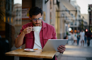 Man crypto investor sips coffee while checking financial data on a tablet at a modern café in...