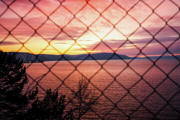 Sunset through the  metal-mesh fence