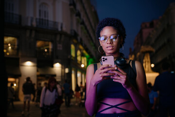 Focused woman using phone in night city, managing finances or checking messages through mobile apps in urban setting