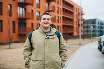 A handsome young man with backpack walking on the street in the city. Urban lifestyle concept. Traveler. Spring time. Portrait of happy young man in casual clothing standing outdoor.