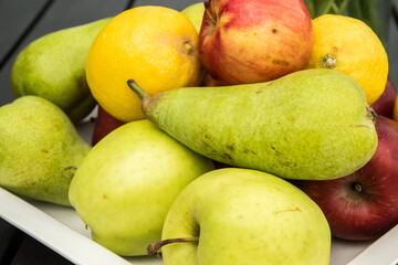 Different types of fruits on a white plate on a black wooden background