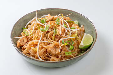 Plate of Pad Thai with rice noodles, vegetables, chicken, and tamarind sauce, served in a green ceramic bowl on a white background. Bright, inviting photo, ideal for Thai and Asian cuisine themes. 

