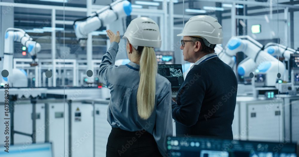 Poster portrait of a male technician and female businesswoman in a factory, talking, using laptop computer 