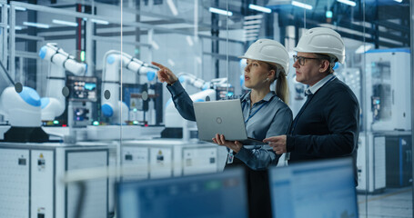 Young Engineer and Technician Having a Conversation and Using a Laptop Computer. Industrial...