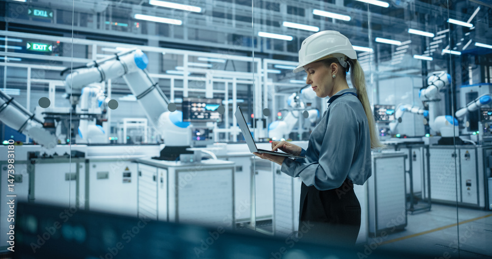 Poster Computer Monitors Display Robotic Operations and Data Analytics. Female Engineer in a Hard Hat Working in an Industrial Facility, Using Laptop Computer to Monitor Robotic Arms in a Futuristic Factory