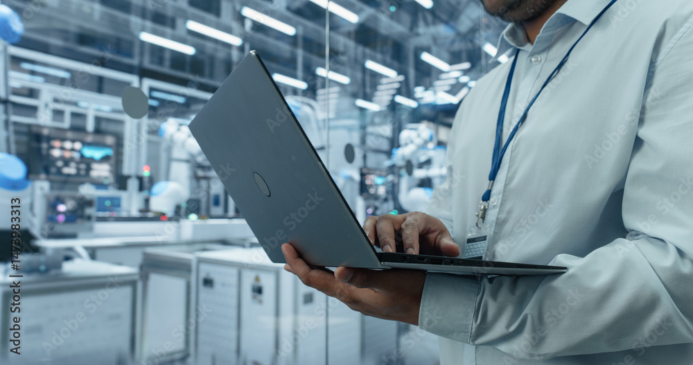 Poster Close Up of an Anonymous Engineer Using a Laptop Computer to Monitor Robotic Arms in an Advanced Industrial Factory. Specialist Overlooking Modern Automated Electronics Manufacturing