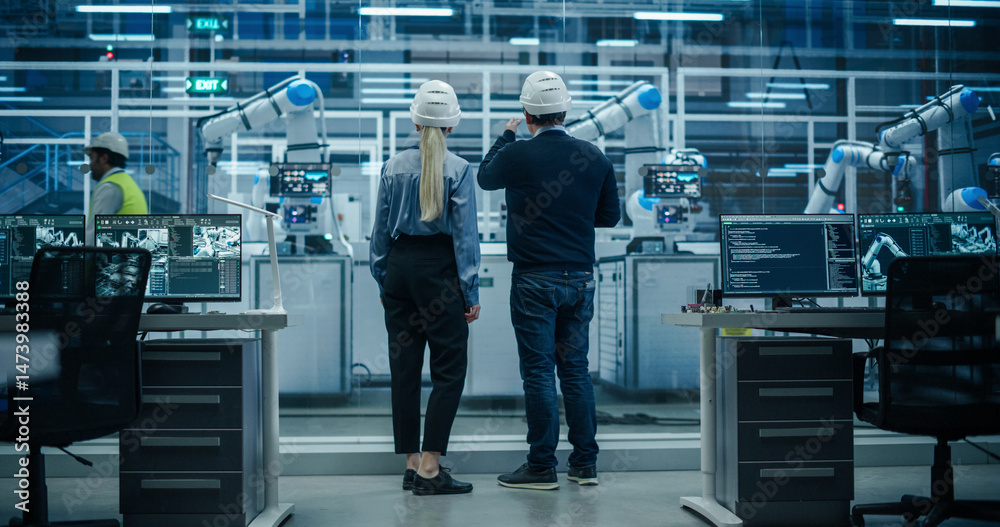 Poster Female and Male Industrial Engineers Having a Conversation at a Modern Tech Electronics Factory with Automated Robot Arms Working with the Help of Artificial Intelligence Software. Back View