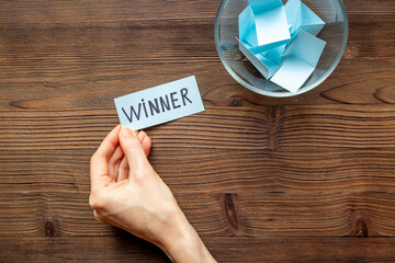 Hand is holding raffle ticket winner near glass jar, top view. Luck and lottery concept