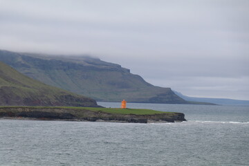 orange lighthouse contrasting agains the green cliffs of the Icelandic coast with a low hanging...