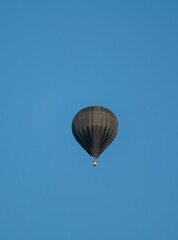 A black hot air balloon is floating in the sky above a blue sky