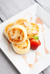 Delicious sweet cottage cheese pancakes served with fresh strawberries and cream on a white plate for breakfast