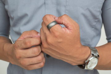 A Southeast Asian man in smart casual wear adjusts a matte gray silicone ring on his finger. Isolated on a light background.