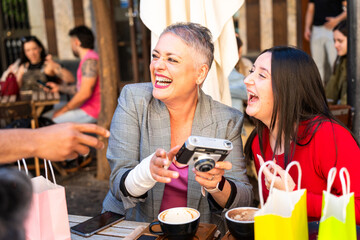 Two cheerful women laughing and holding a vintage camera at a cafe table