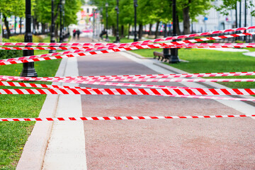 Red and white caution tape stretched across park walkway, restricted access or area under...