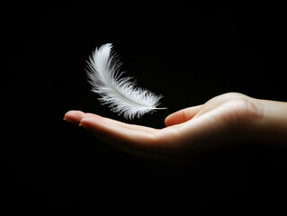 White feather floating gently above an outstretched hand in darkness