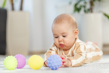 Baby explores colorful balls on soft carpet in bright living room. Five-month-old baby. Copy space