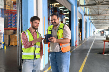 Two Warehouse worker in safety uniform check the stock order details and goods supplies in the...