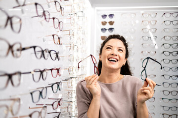 Beautiful smiling girl choosing new eyeglasses in optician store.