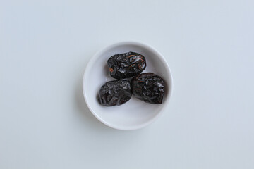 Three pieces of ajwa dates or ajwa khajur, in small bowl, isolated on white background, flat lay or top view