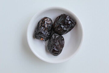 Three pieces of ajwa dates or ajwa khajur, in small bowl, isolated on white background, flat lay or top view