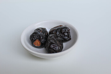 Three pieces of ajwa dates or ajwa khajur, in small bowl, isolated on white background